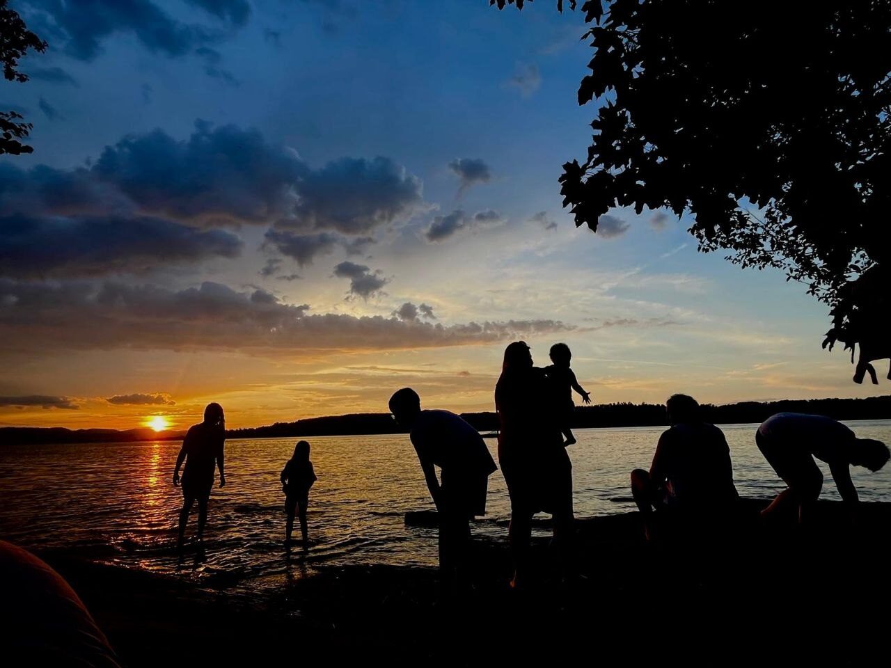 Silhouetten von Menschen am See bei Sonnenuntergang